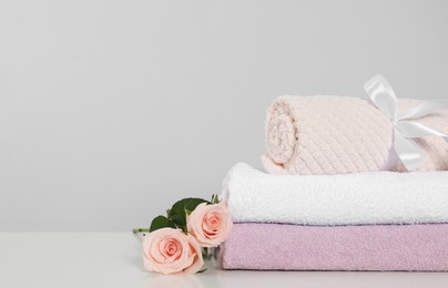 Photo of Clean soft towels with flowers on white table against light grey background. Space for text