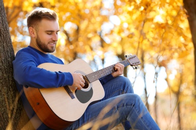 Young man playing guitar in autumn park