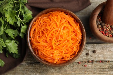 Photo of Delicious Korean carrot salad, parsley and spices on wooden table, flat lay