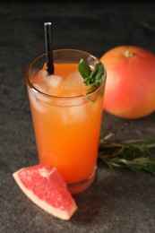 Photo of Tasty grapefruit drink with ice and mint in glass on dark textured table