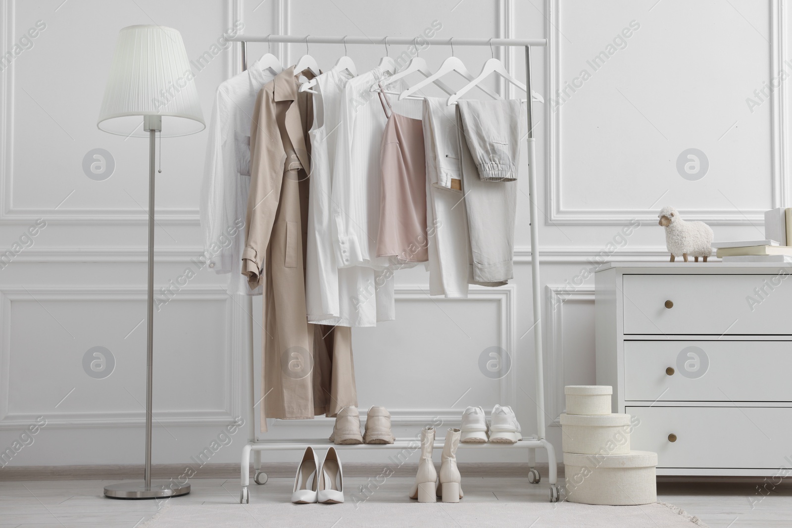 Photo of Rack with different stylish women`s clothes, shoes, lamp and dresser near white wall in room