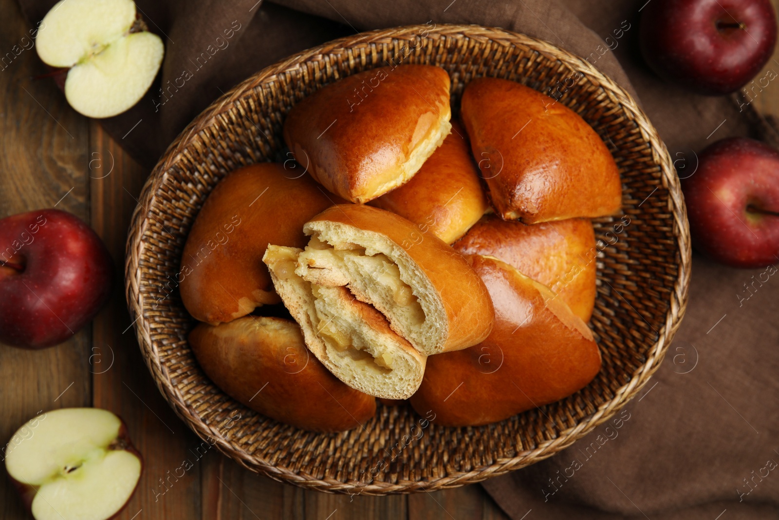 Photo of Delicious baked apple pirozhki in wicker basket and fruits on wooden table, flat lay