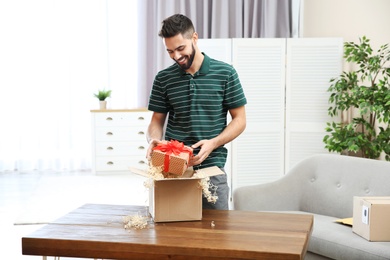 Young man opening parcel on table at home