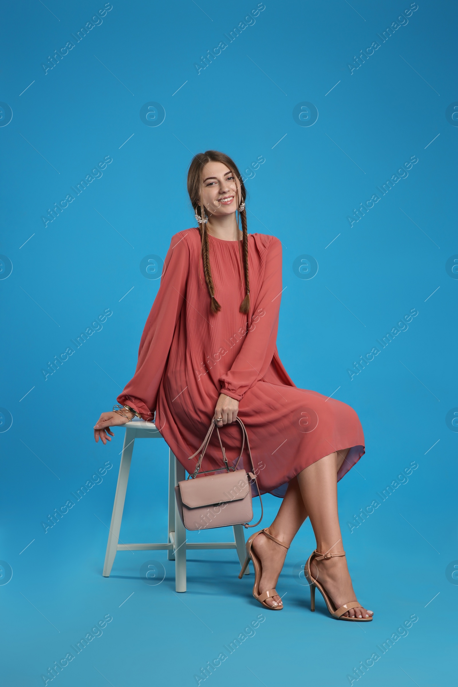 Photo of Beautiful young woman with stylish pink bag on light blue background