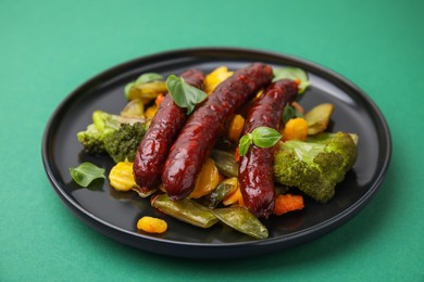 Delicious smoked sausage and baked vegetables on green background, closeup