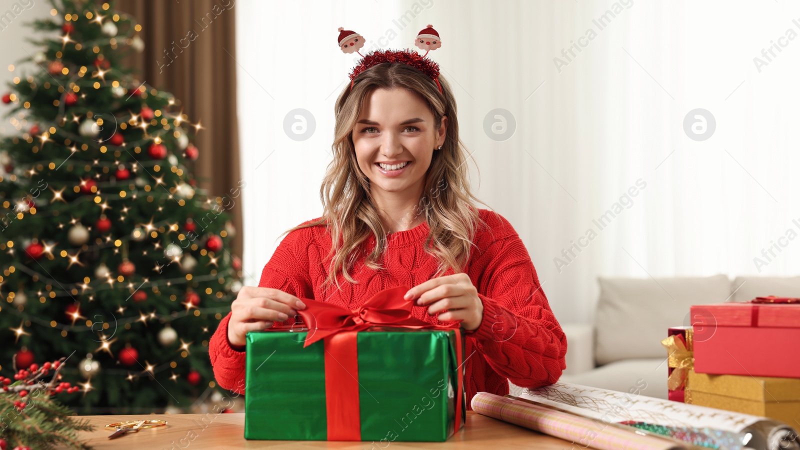 Photo of Beautiful young woman wrapping Christmas gift at home