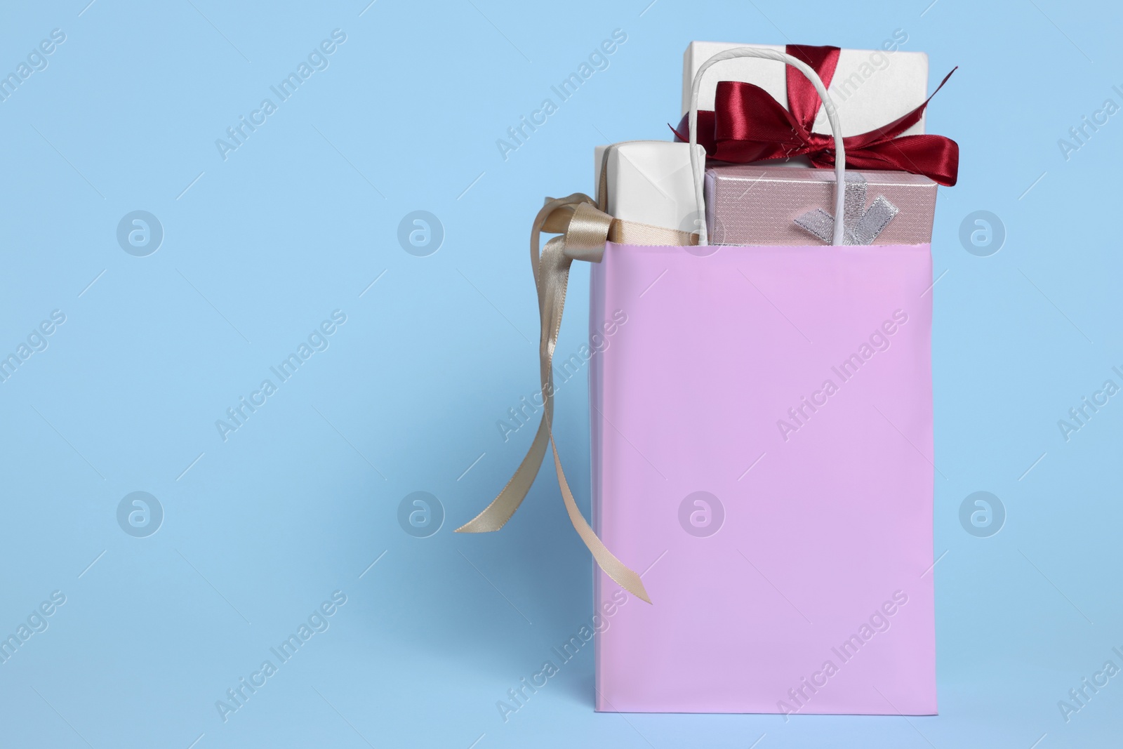 Photo of Pink paper shopping bag full of gift boxes on light blue background. Space for text