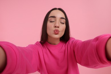 Photo of Young woman taking selfie and blowing kiss on pink background