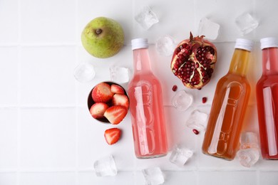 Tasty kombucha in glass bottles, fresh fruits and ice on white table, flat lay. Space for text