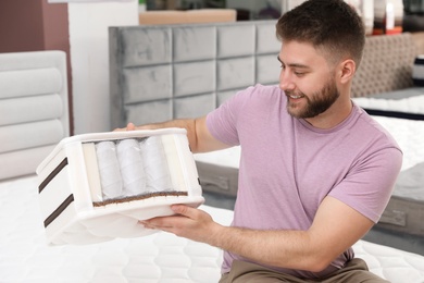 Photo of Smiling man holding sample of orthopedic mattress in store