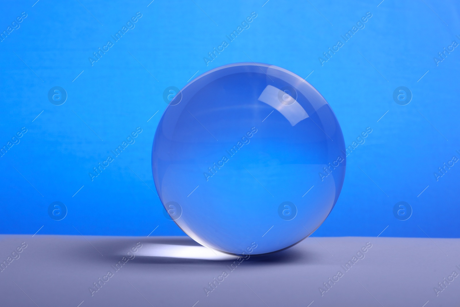 Photo of Transparent glass ball on table against blue background