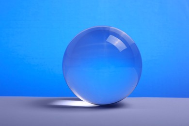 Transparent glass ball on table against blue background