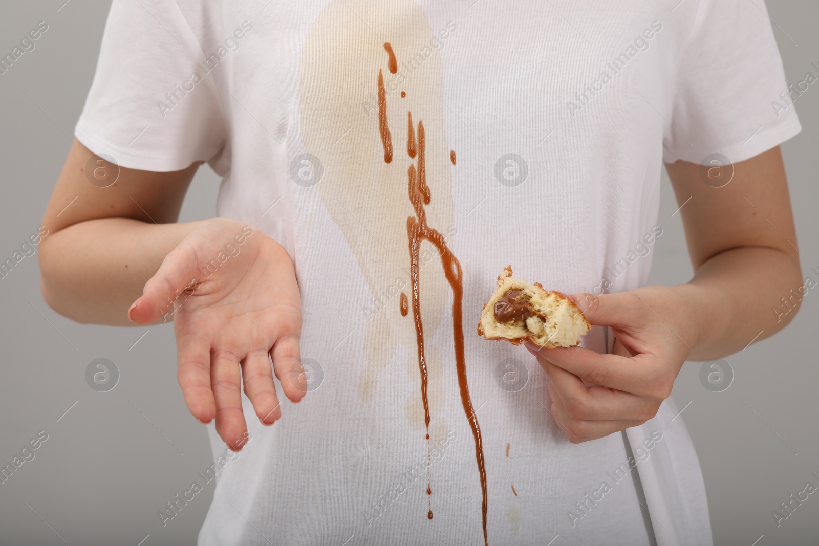 Photo of Woman holding pastry and showing stain from condensed milk on her shirt against light grey background, closeup