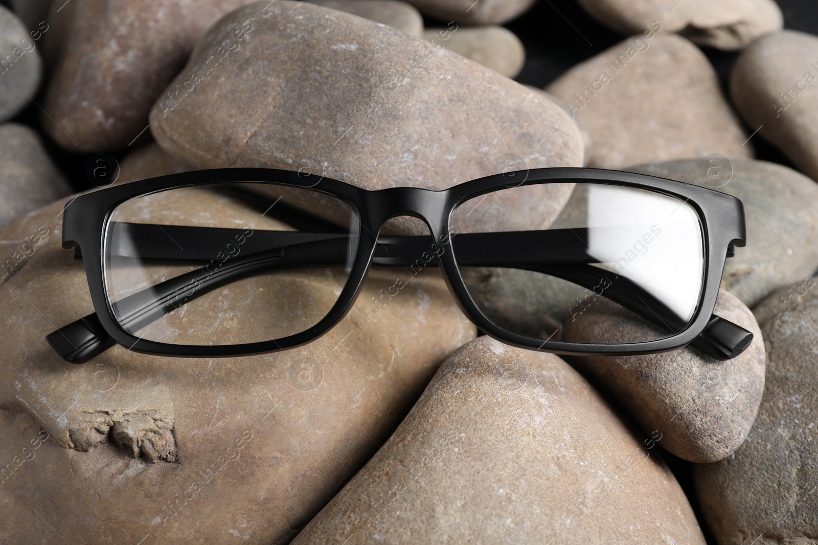 Photo of Glasses in stylish black frame on stones, closeup