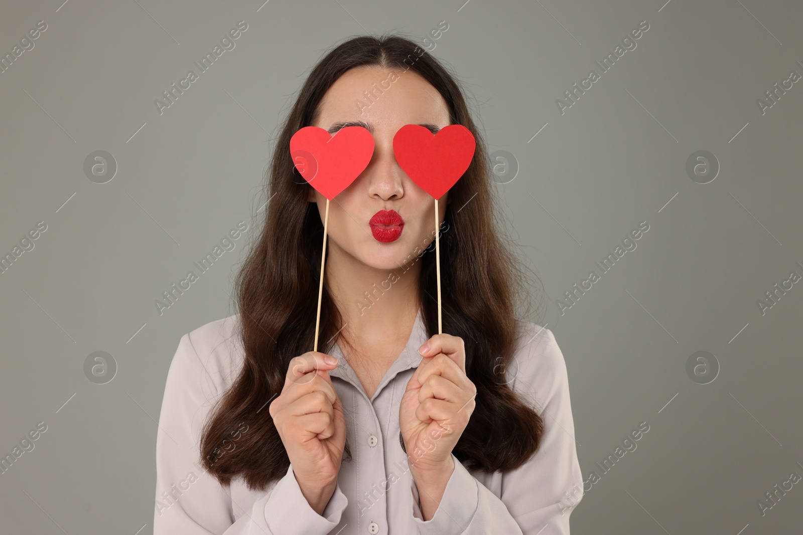 Photo of Young woman covering her eyes with paper hearts on grey background