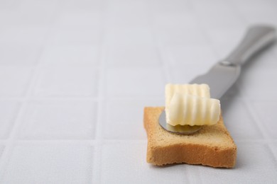 Photo of Tasty butter curl, knife and piece of dry bread on white tiled table, closeup. Space for text