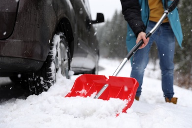 Photo of Man cleaning snow with shovel near stuck car outdoors