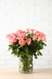 Photo of Vase with beautiful rose flowers on table against brick wall background