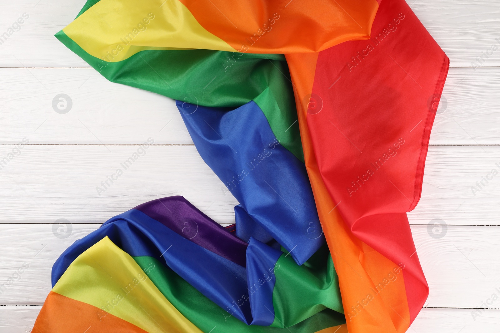 Photo of Rainbow LGBT flag on white wooden table, top view