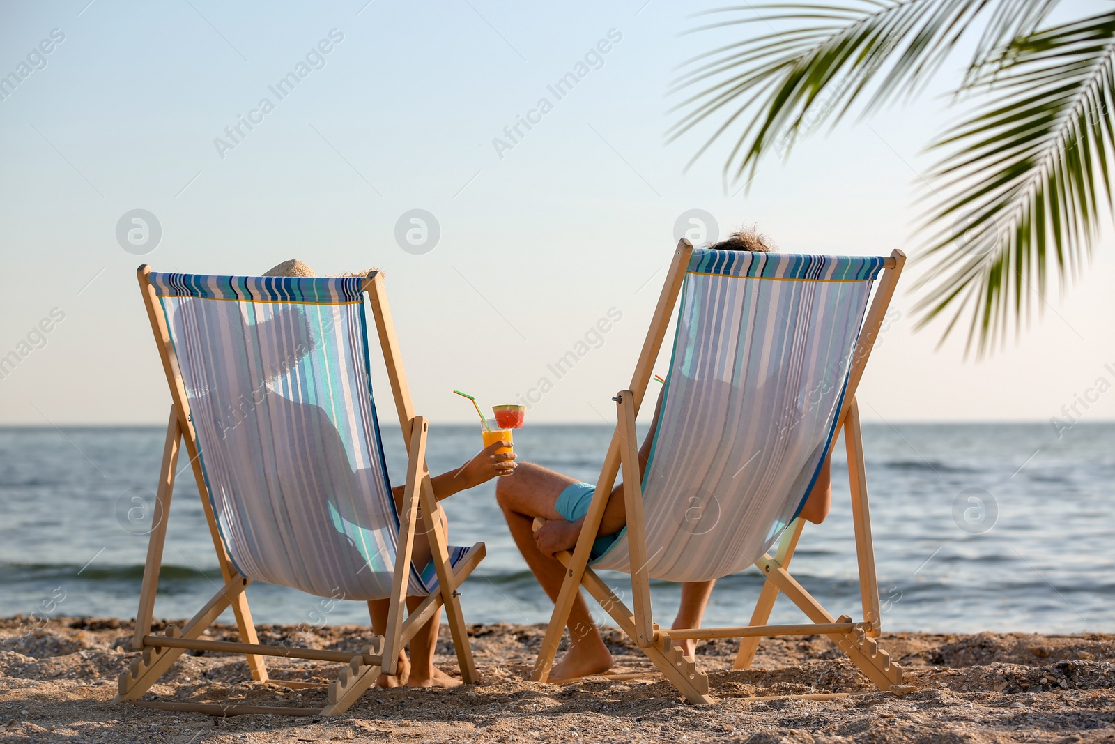 Photo of Young couple with cocktails in beach chairs at seacoast