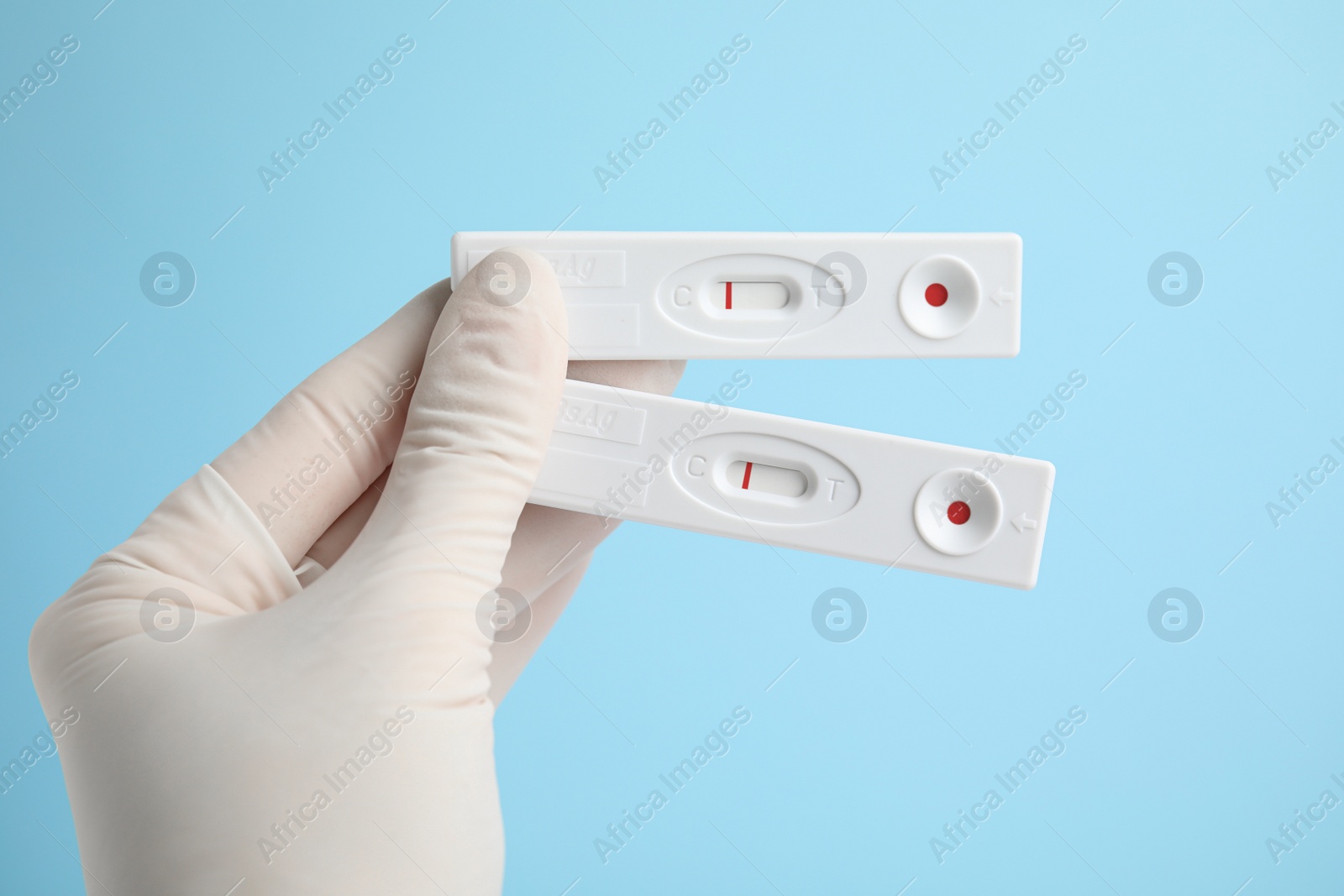 Photo of Doctor holding two disposable express tests for hepatitis on light blue background, closeup