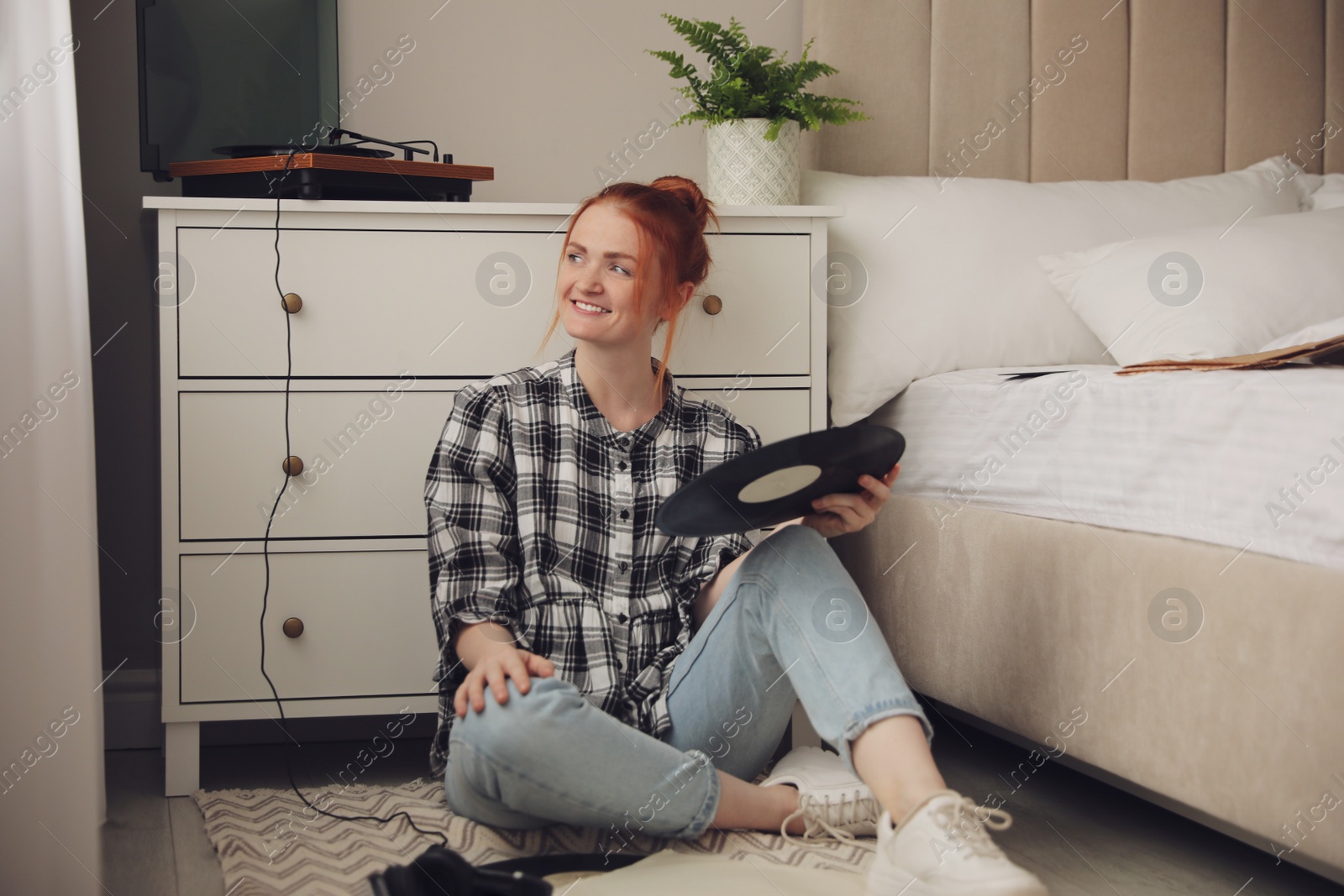 Photo of Young woman choosing vinyl disc to play music with turntable in bedroom