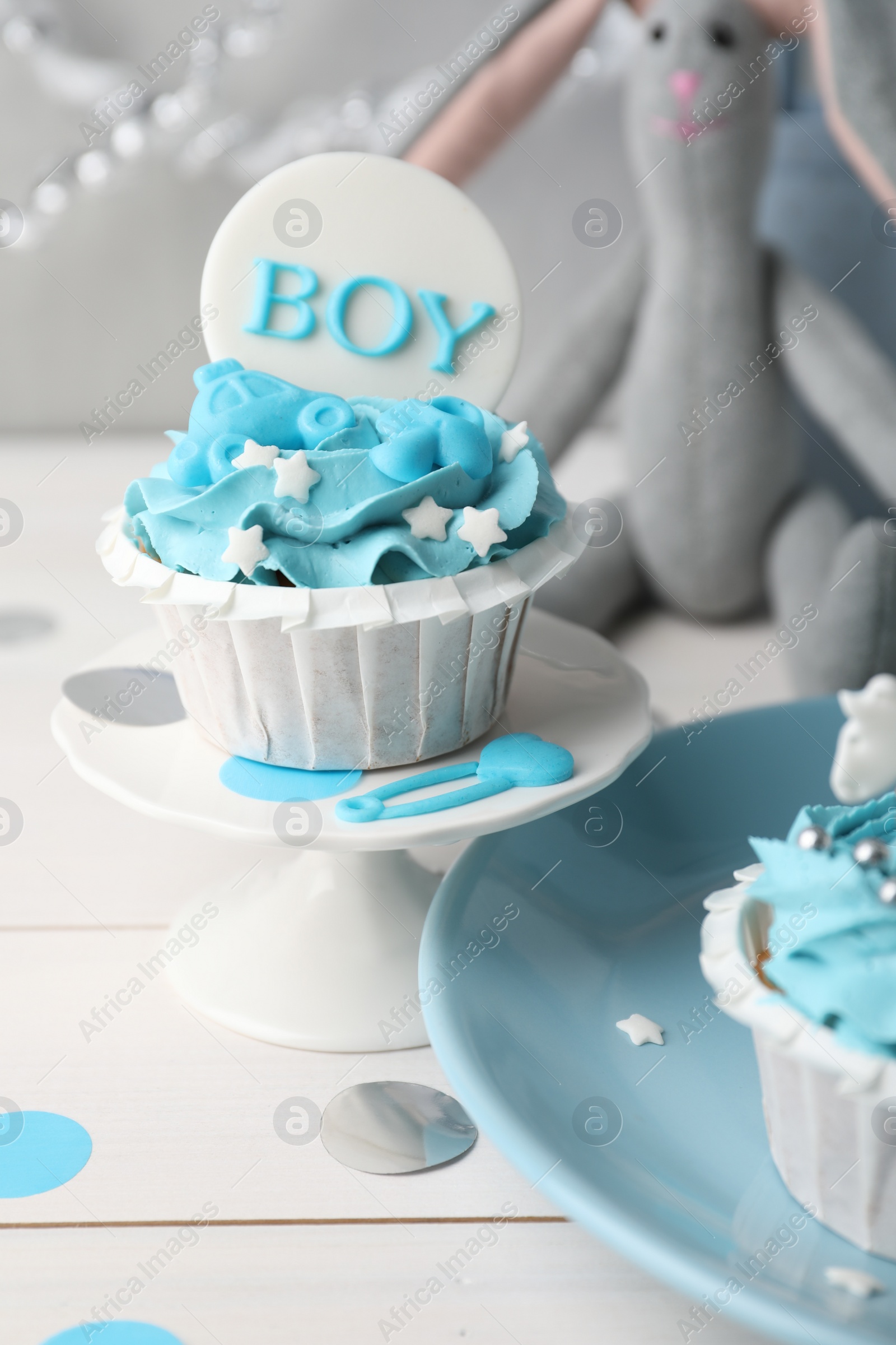 Photo of Delicious cupcake with light blue cream and Boy topper for baby shower on white wooden table