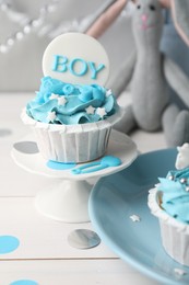 Photo of Delicious cupcake with light blue cream and Boy topper for baby shower on white wooden table