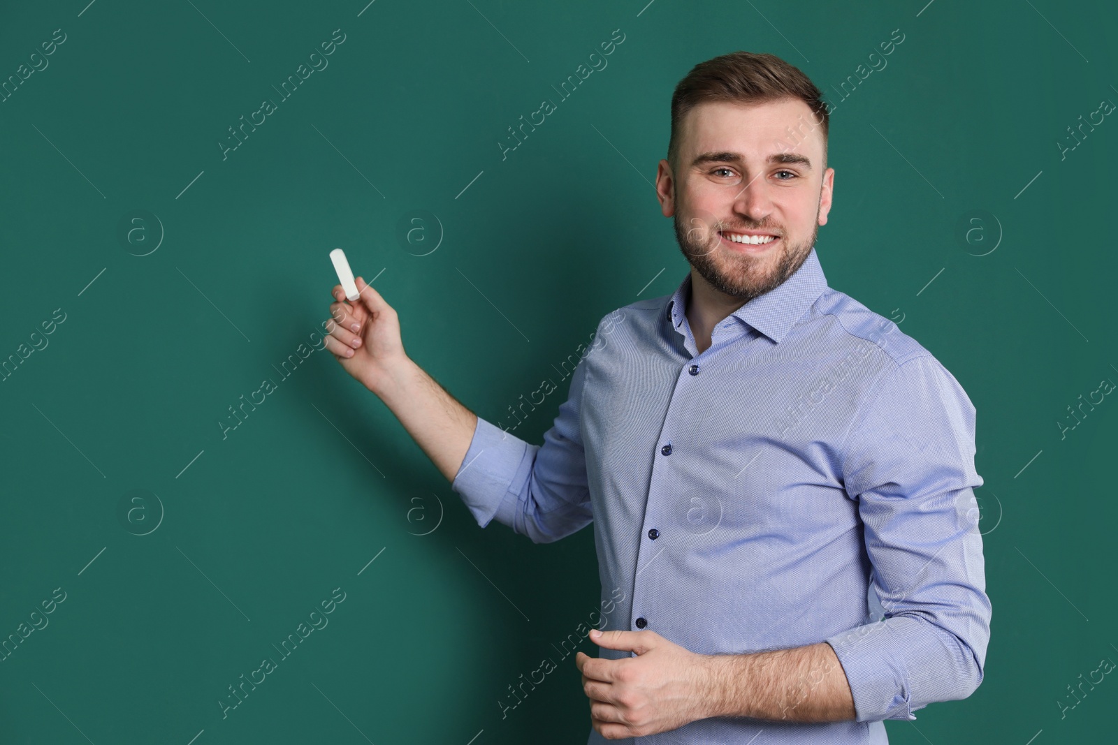 Photo of Portrait of young teacher with chalk on green background. Space for text