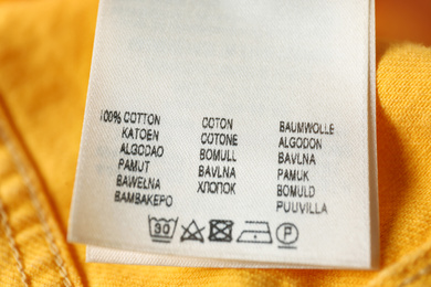 Photo of Clothing label with care symbols and material content on yellow jeans, closeup view