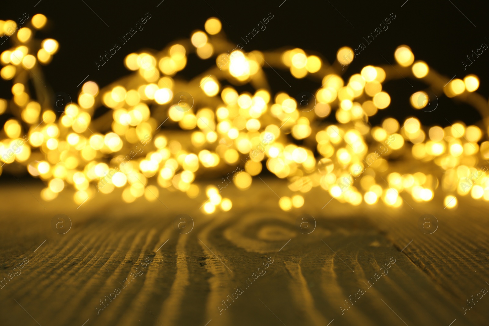 Photo of Beautiful glowing Christmas lights on wooden surface, blurred view