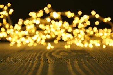 Beautiful glowing Christmas lights on wooden surface, blurred view