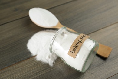Photo of Overturned jar and spoon with baking soda on wooden table, closeup