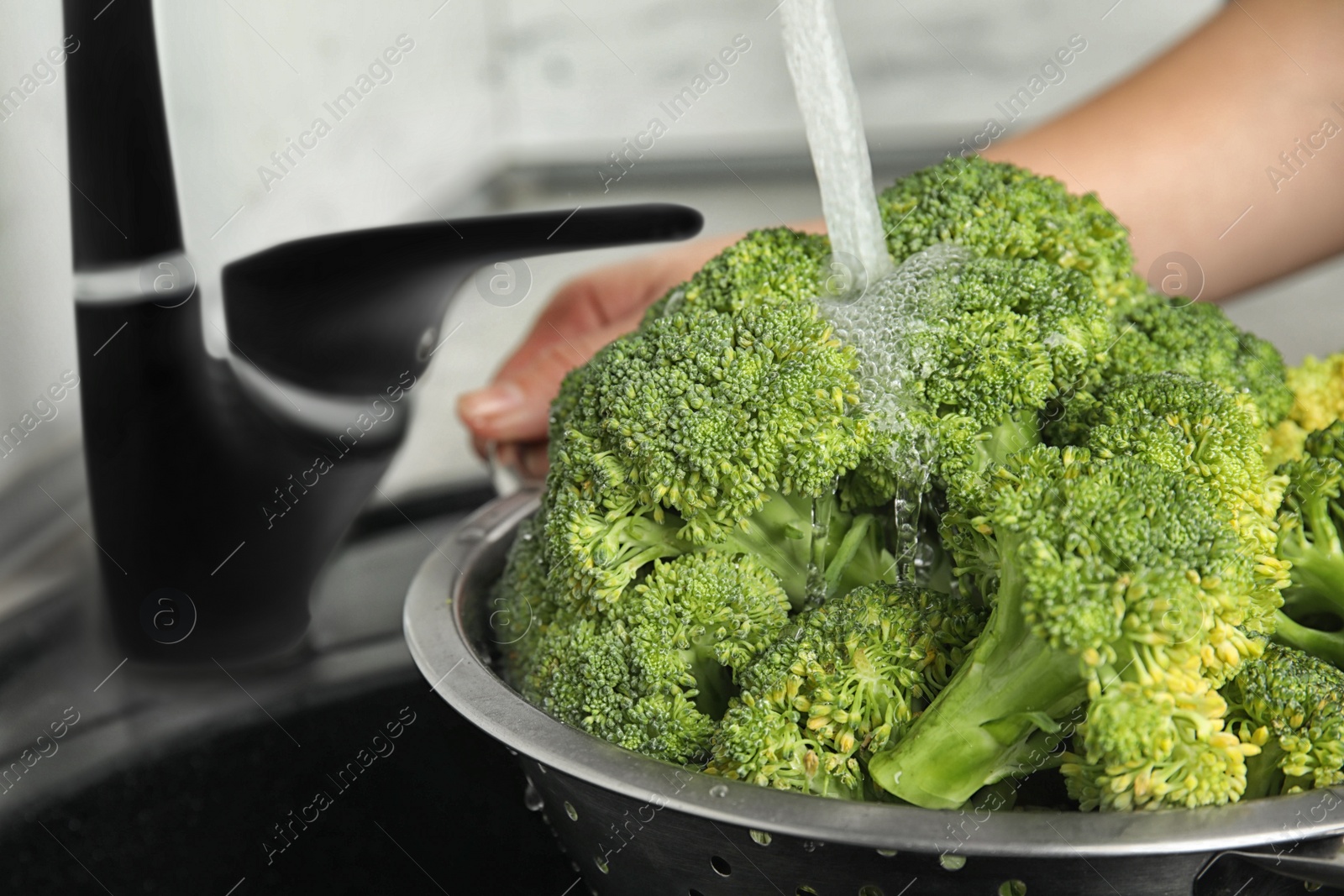 Photo of Woman washing fresh green broccoli in kitchen sink, closeup