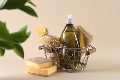 Bottle of cleaning product, sponges, brushes and floral decor on beige background