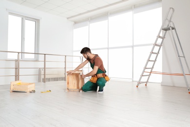 Photo of Handyman in uniform assembling furniture indoors. Professional construction tools