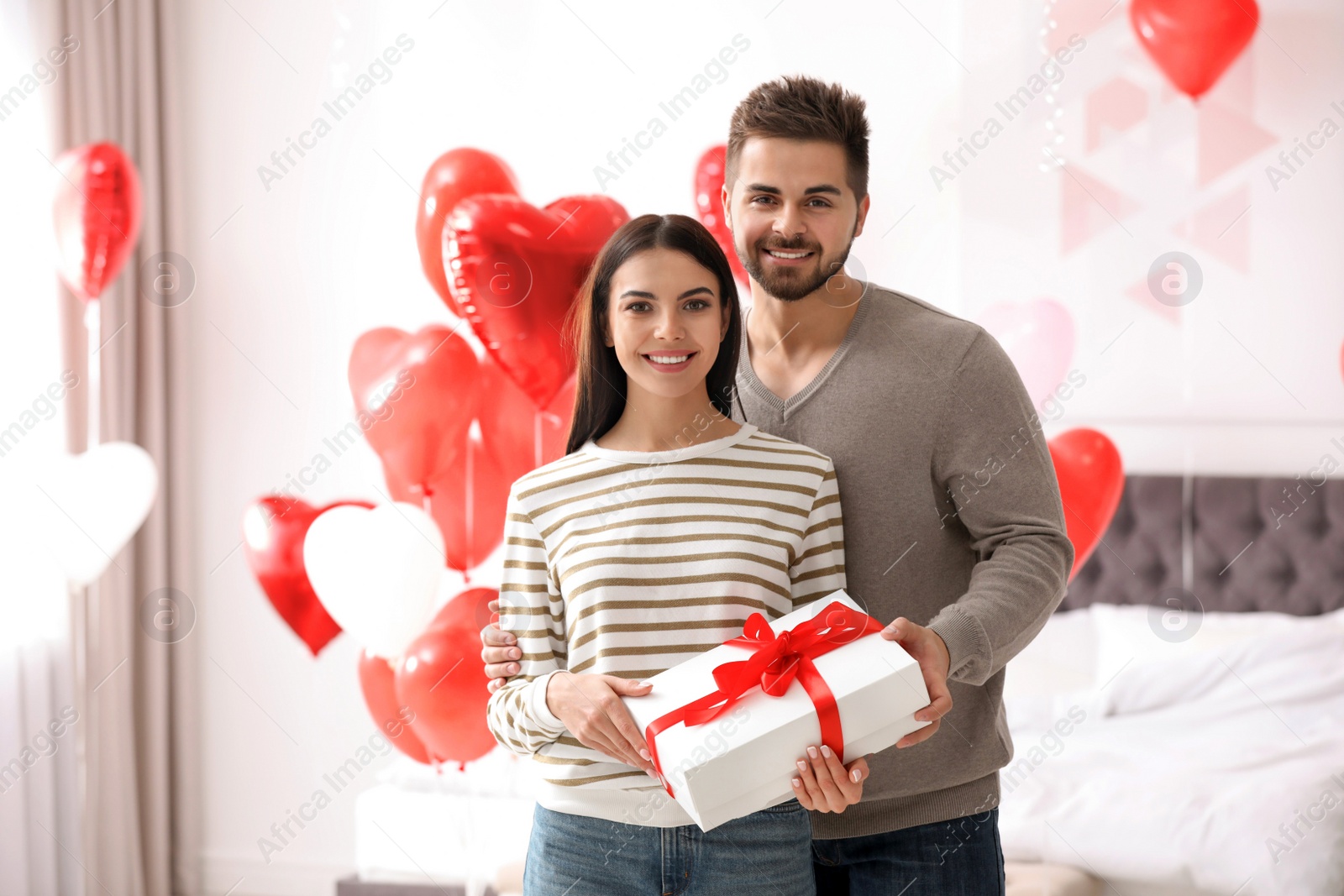 Photo of Happy young couple in bedroom decorated with heart shaped balloons. Valentine's day celebration