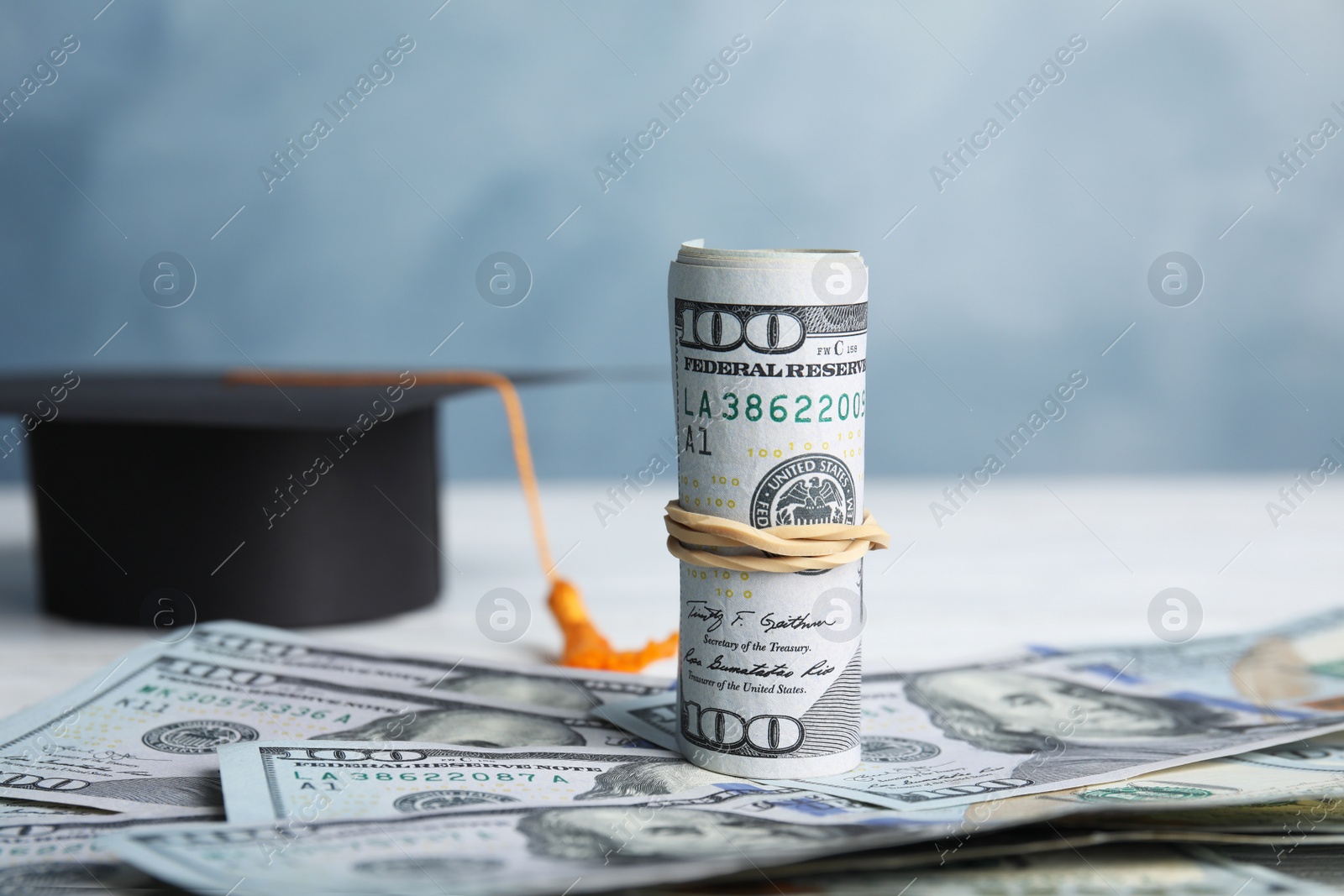 Photo of Dollar banknotes and student graduation hat on white wooden table against blue background. Tuition fees concept