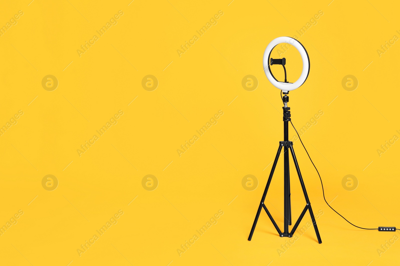 Photo of Modern tripod with ring light on yellow background. Space for text