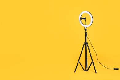 Photo of Modern tripod with ring light on yellow background. Space for text