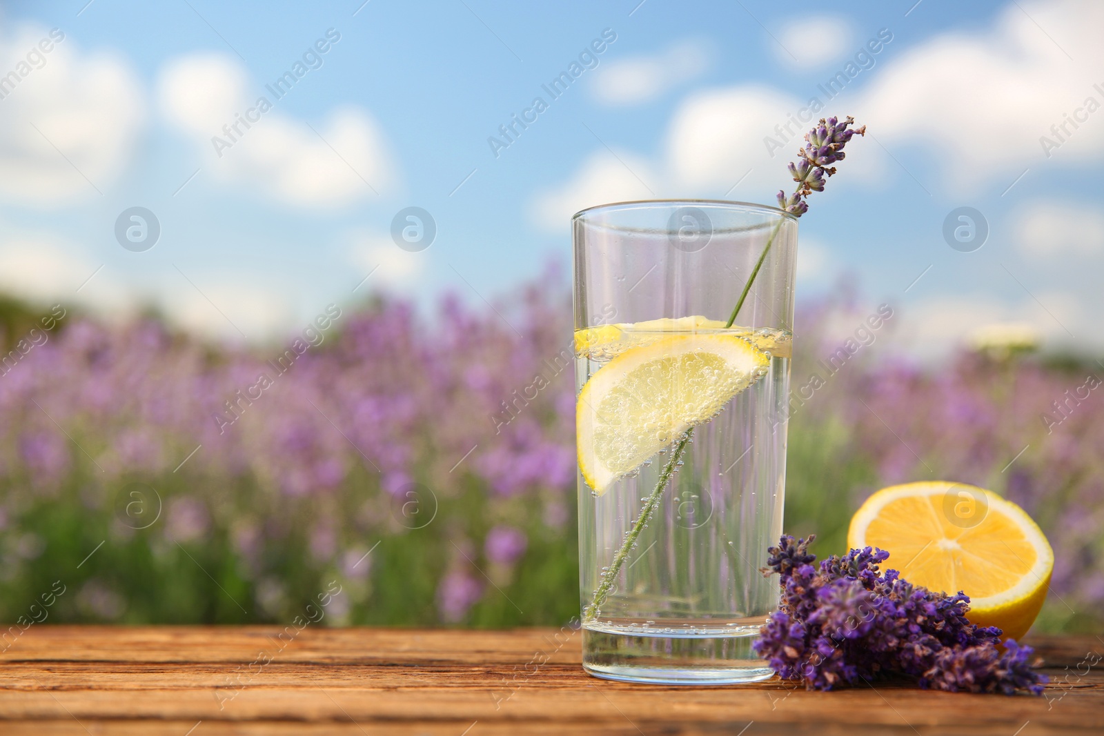 Photo of Lemonade with lemon slices and lavender flowers on wooden table outdoors, closeup. Space for text