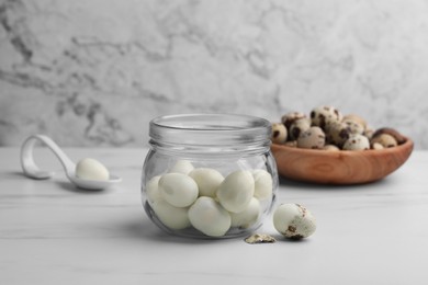Glass jar with peeled boiled quail eggs and another one partly in shell on white table