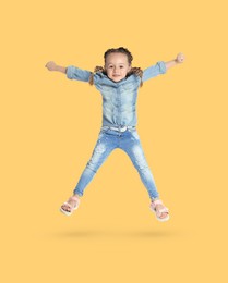 Happy cute girl jumping on light golden background