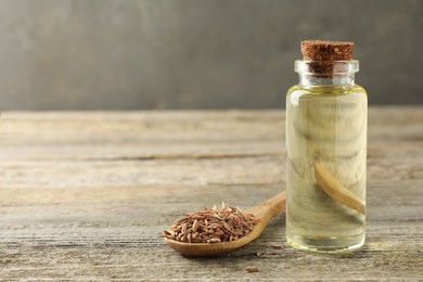 Spoon of caraway (Persian cumin) seeds and essential oil on wooden table, space for text