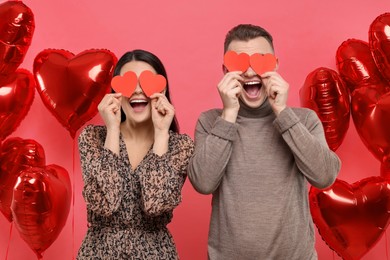 Photo of Lovely couple holding paper hearts near heart shaped air balloons on red background. Valentine's day celebration