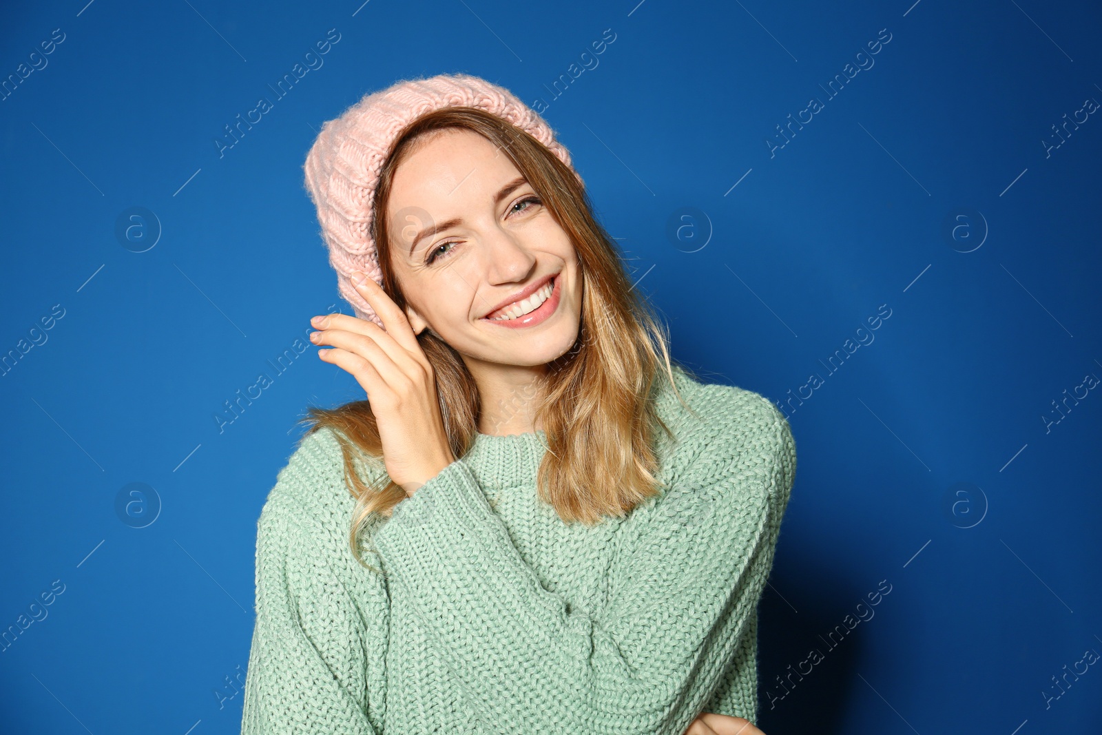 Image of Happy young woman wearing warm sweater and knitted hat on blue background