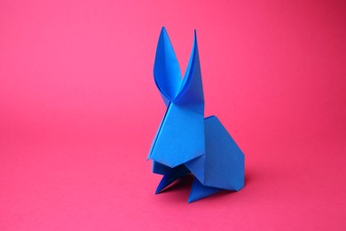 Photo of Light blue paper bunny on pink background, space for text. Origami art