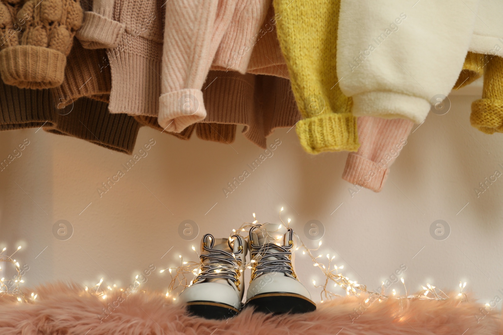 Photo of Pair of stylish female boots and different warm clothes indoors