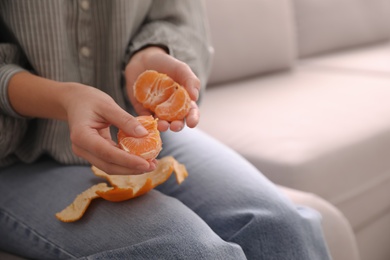 Woman with tasty fresh tangerine on sofa, closeup