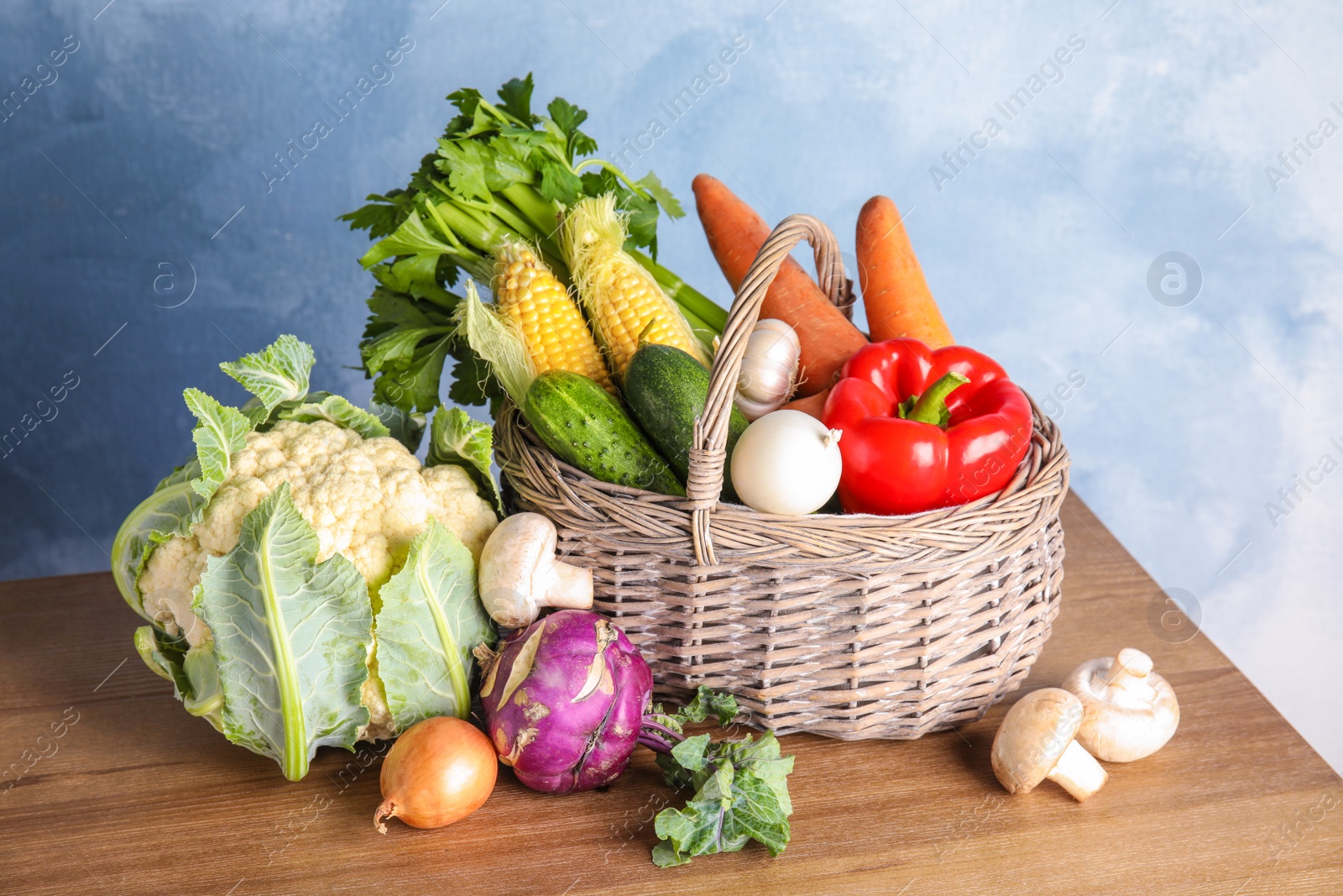 Photo of Basket full of fresh healthy vegetables on table against color background